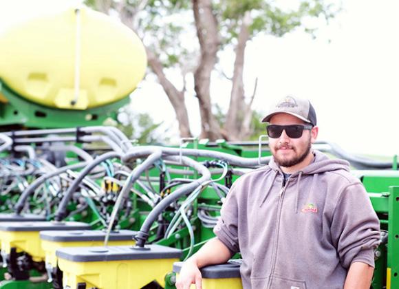 Alex Millershaski stands next to a seed planter used for crops like wheat, corn and sorghum. Calen Moore/Kansas News Service