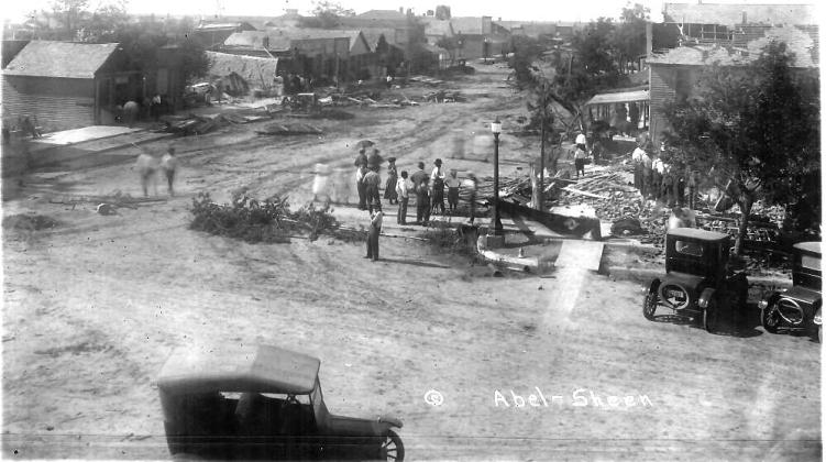Above: The view of the main intersection in Leoti looking North. The rubble everyone is looking at used to be the two-story brick Leoti Mercantile Company building (sometimes known as the Koontz and Jones store). In its place would eventually be built the cast-concrete structure that now houses The Native Sun.