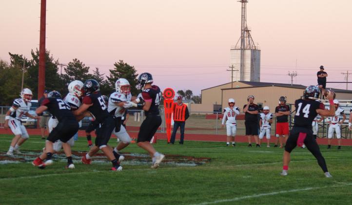 Cashton Young (14) prepares to throw the football as Holden Whalen (25), Zane Gerstberger (59), and Chase Carpenter (42) provide blocking protection in the Oct 17 game against Quinter.