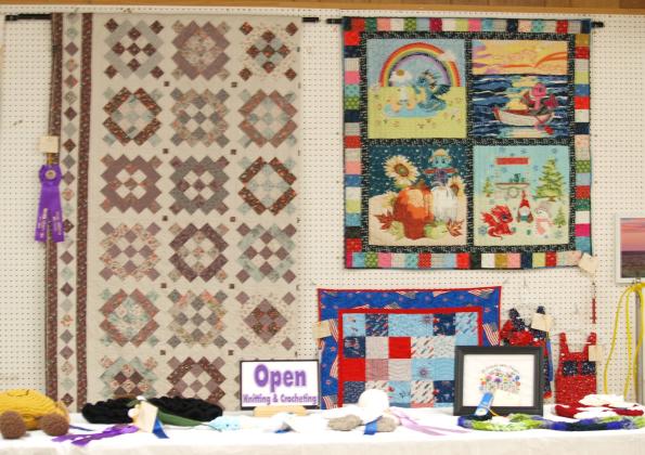 Opening knitting and crocheting displays on the table, quilts on the wall.