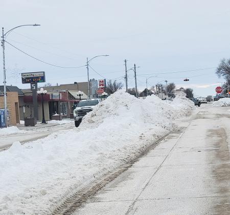 This staff photo taken Thursday, January 11, shows how tall the snow piles are in the middle of 4th street, especially at the intersections, shown here in front of Leoti Foods.