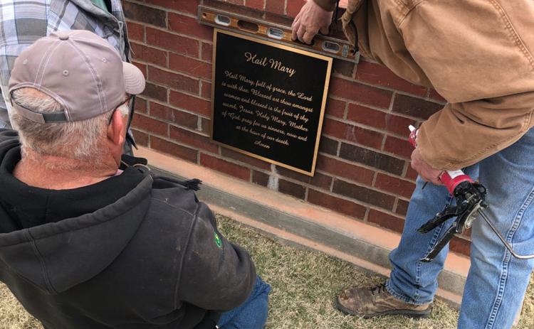 Chris Kreutzer, Gary Graff (back to camera) and Mike Berend install a plaque with the words of the Hail Mary prayer on the pedestal of the statue of Mary at St. Mary Cemetery in Marienthal. It is part of ongoing improvement projects at the cemetery.