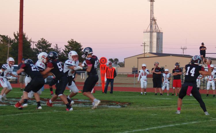 Cashton Young (14) prepares to throw the football as Holden Whalen (25), Zane Gerstberger (59), and Chase Carpenter (42) provide blocking protection in the Oct 17 game against Quinter.