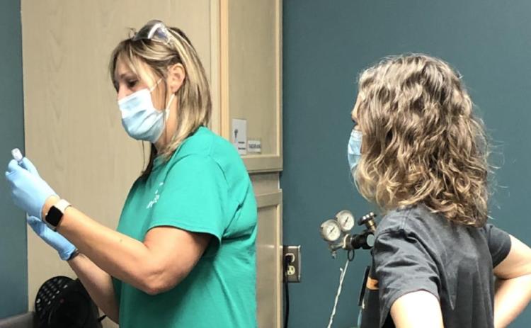 Above: Mindi Bremer fills a syringe with vaccine from a tiny vial. Dr. Julia Myers (right) received the first dose.