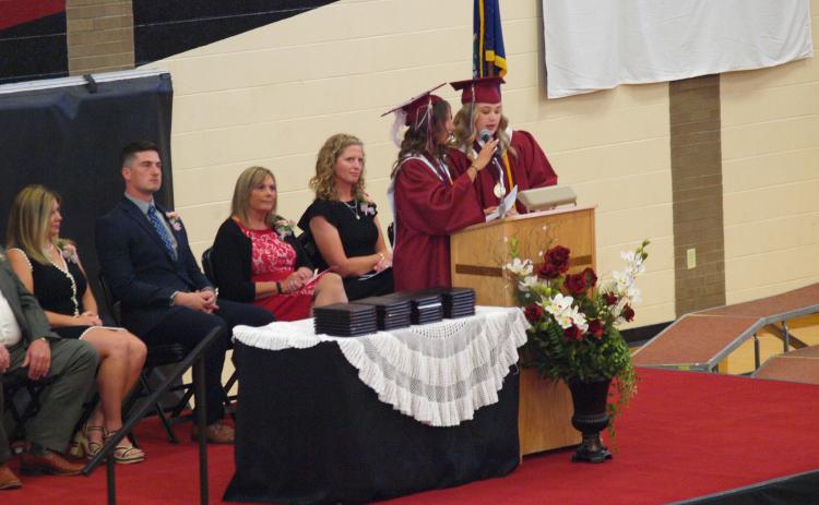 At the Podium (L-R): Salutatorian Jentri Porter and Valedictorian Delaney Biel. Seated (in frame) on the stage: Board of Education President Eryka Smith, WCJSHS Principal Brant Douglas, Superintendent Lori Maxwell, Mrs. Bridgette Carpenter.